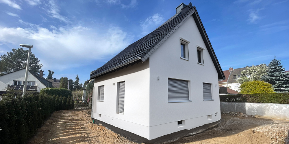 Freistehendes Einfamilienhaus, bei dem das Fundament freigelegt und trockengelegt wurde. Die Fassade ist weiß gestrichen, der Sockel auch. Das Fundament ist mit Erdreich bedeckt.